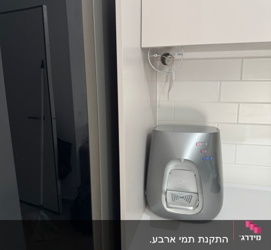 מכשיר מים על משטח מטבח ליד מקרר